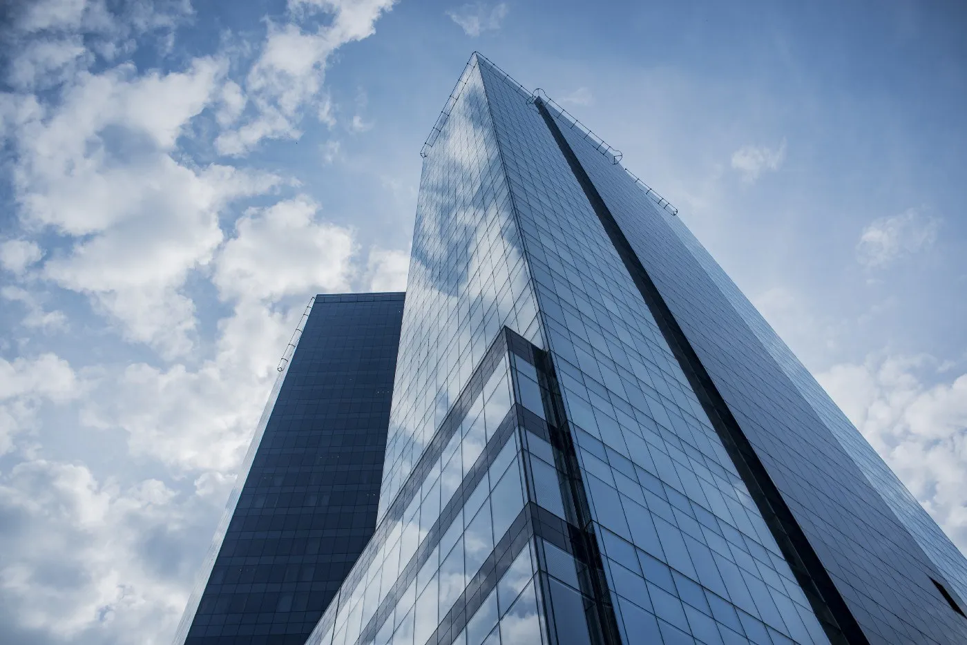 Glass office tower reflecting a blue sky and clouds